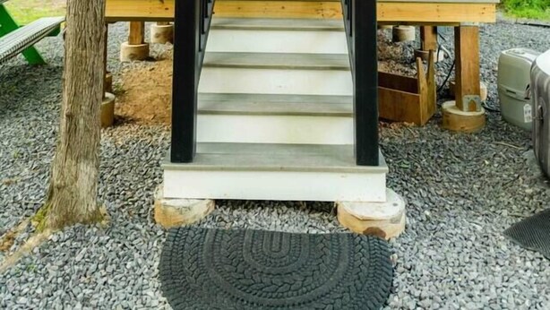 A cabin with a wooden deck, a staircase leading to a door, and a forested background.