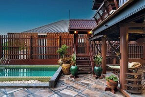 Uma área de piscina com deck ladrilhado, cercas de madeira e plantas em vasos.