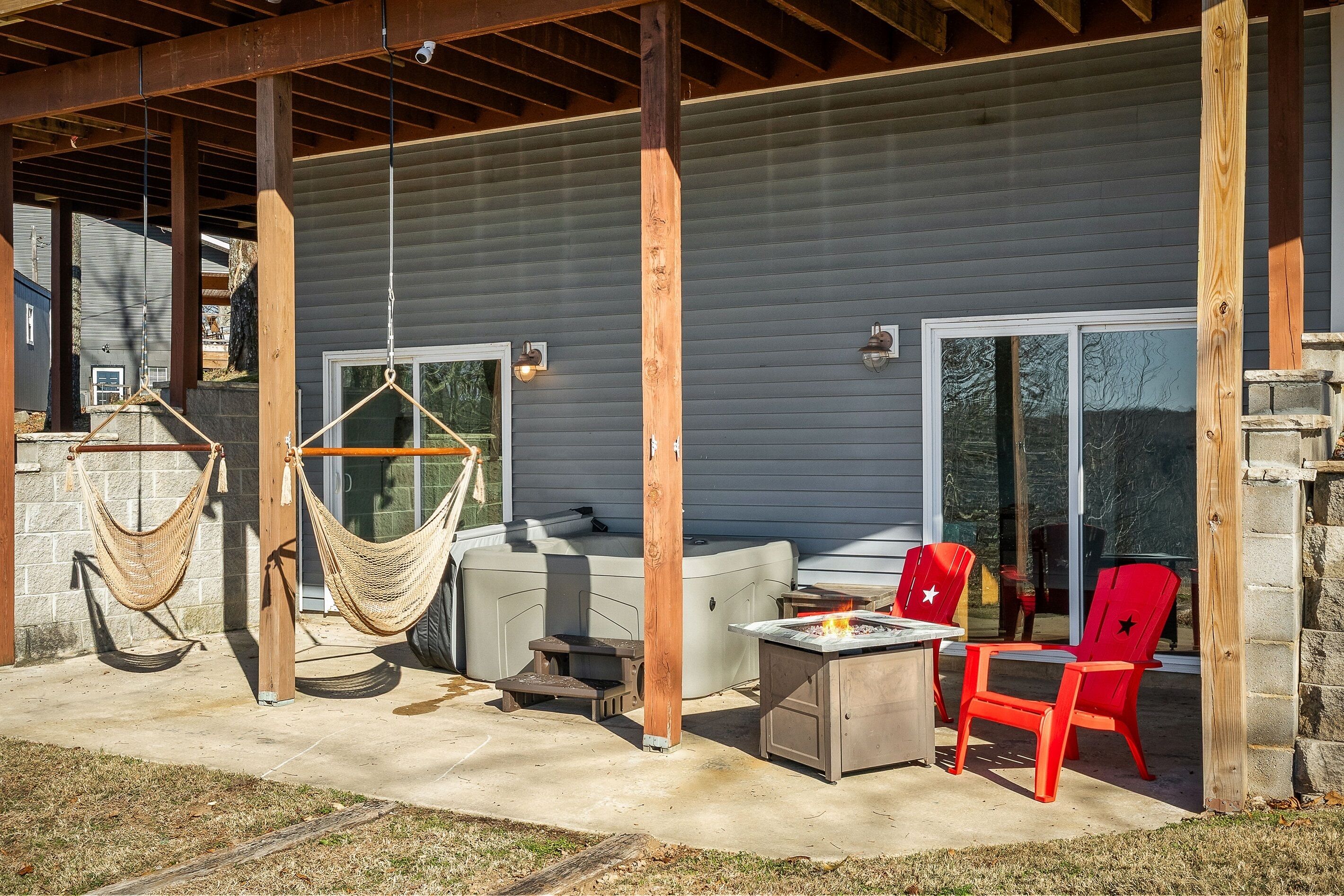 A covered patio with a fire pit, red chairs, a beige sofa, and two hammocks.