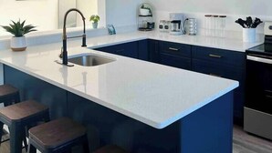 A modern kitchen with a central island, bar stools, a sink, and a coffee maker.
