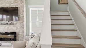 A staircase with wooden steps and a white handrail, a flat-screen TV mounted on a brick wall, and a window with white blinds. - Water Views + Pool Access | Driftwood Cottage (Navarre Beach)