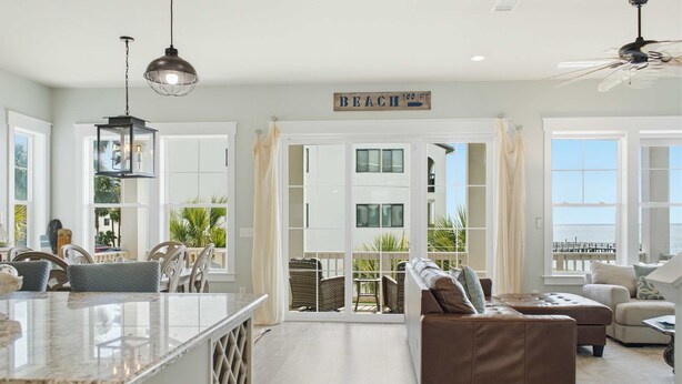 A spacious living area with a large window, a ceiling fan, and a sign that reads 'BEACH 100 FT.' - Water Views + Pool Access | Driftwood Cottage (Navarre Beach)