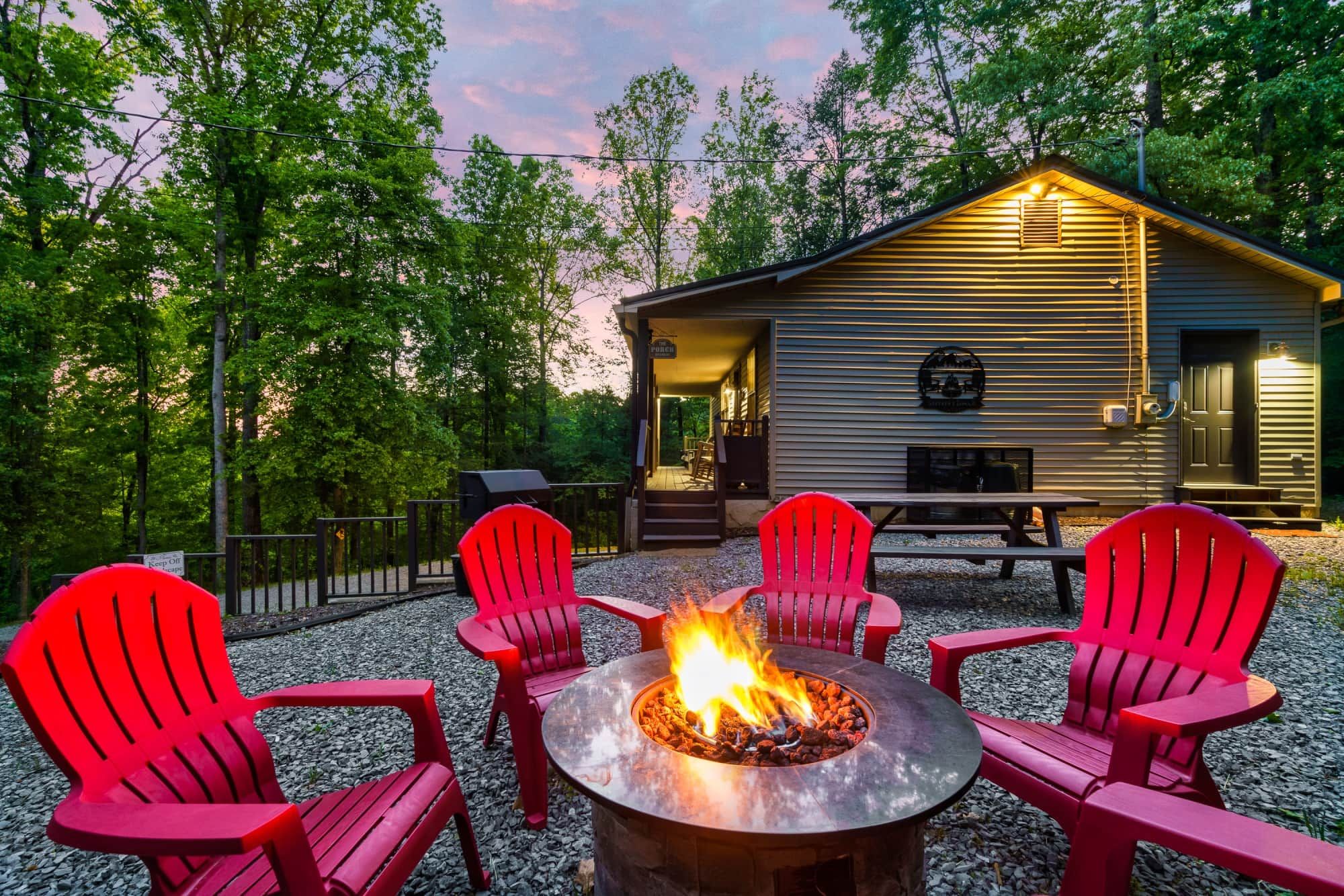 A cabin with a fire pit, red Adirondack chairs, and a bench.