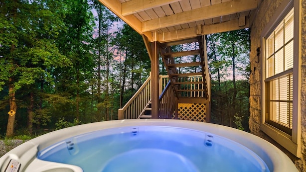 Uma banheira de hidromassagem numa área arborizada, com um deck de madeira e escadas que levam a uma casa.