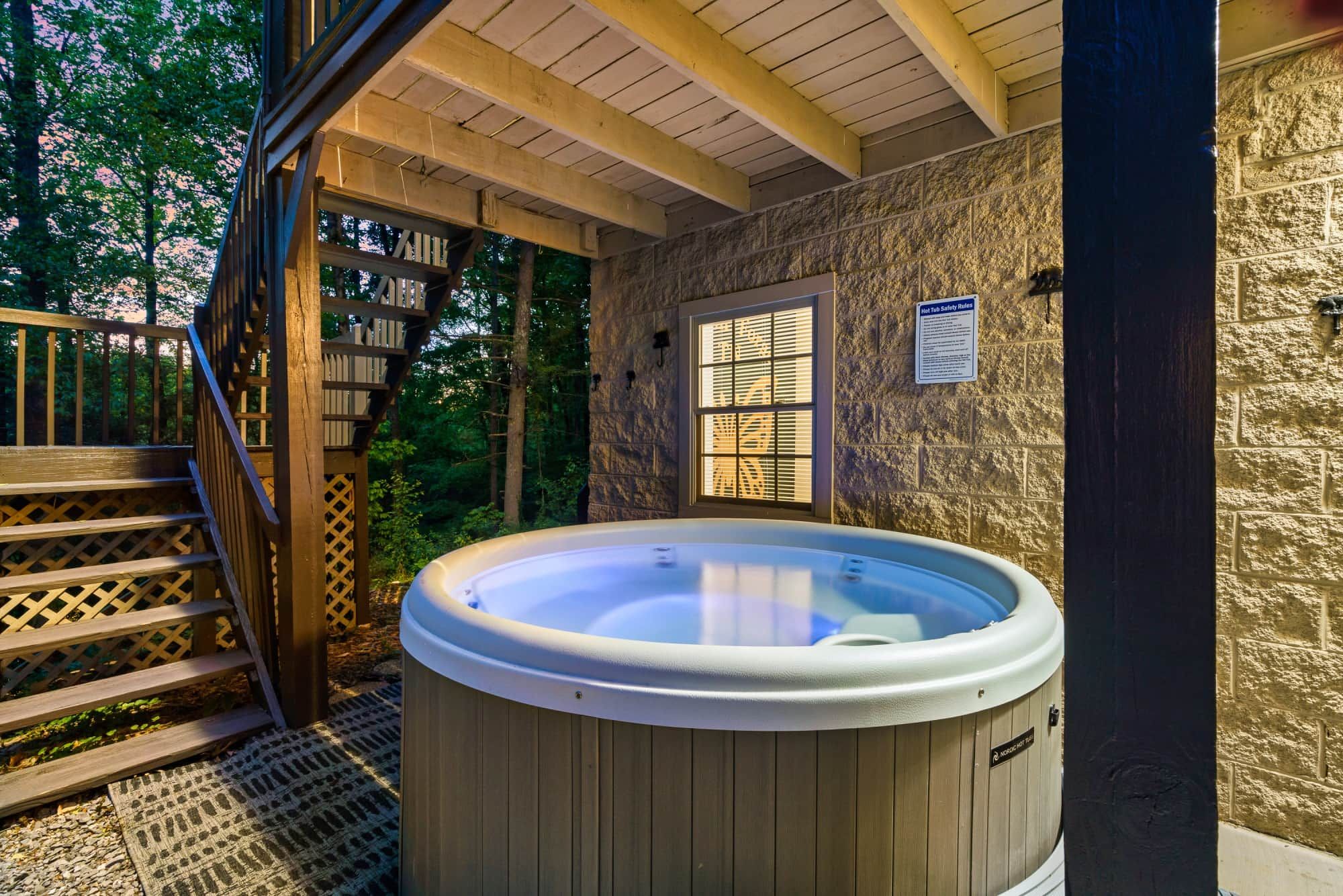 Een jacuzzi in een overdekte buitenruimte met houten traptreden en een stenen muur.