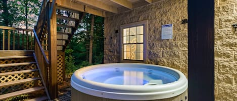 Een jacuzzi in een overdekte buitenruimte met houten traptreden en een stenen muur.