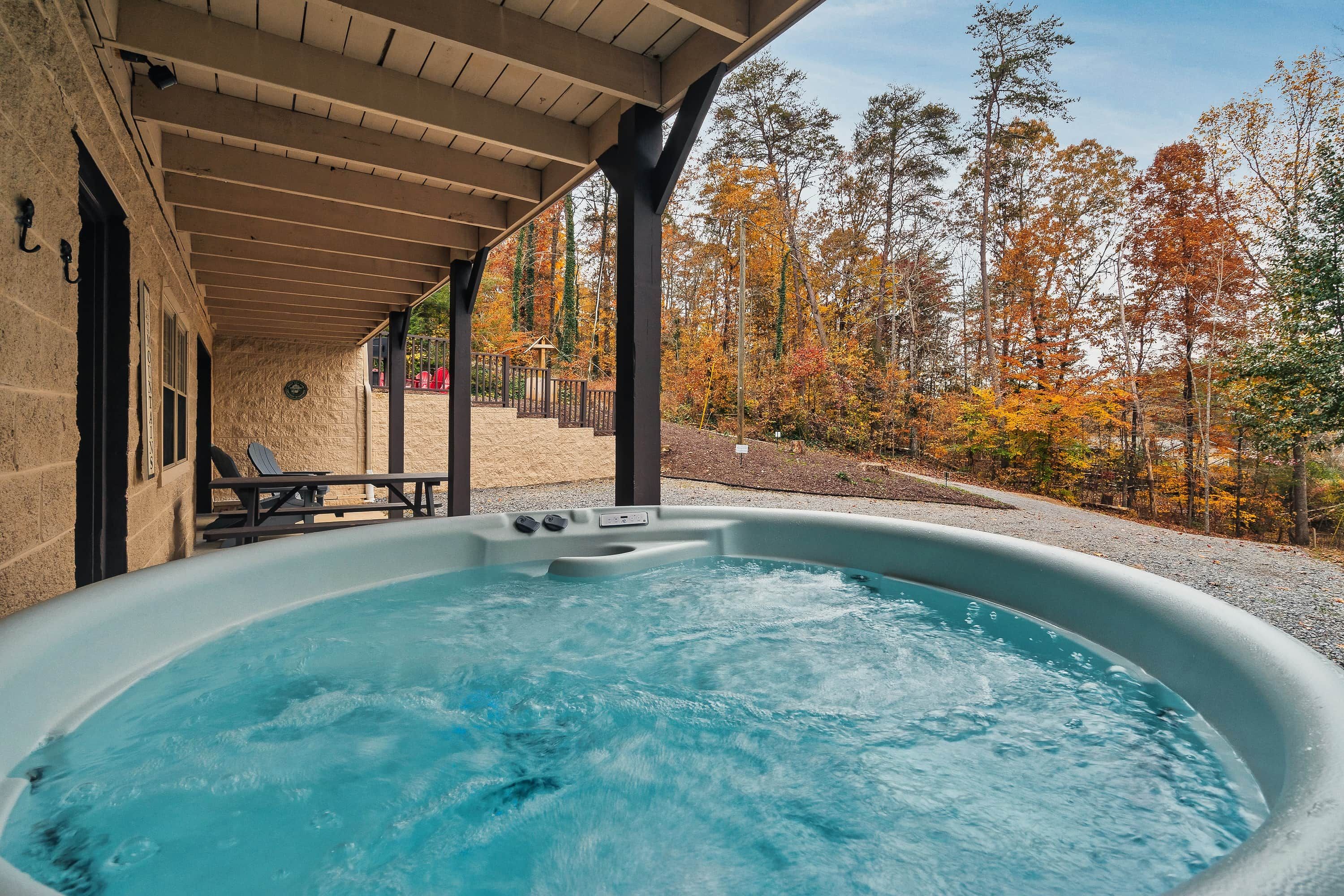 A hot tub under a covered patio with a view of autumn trees.