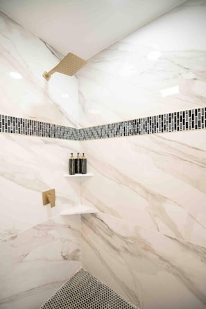 Ein Badezimmer mit Dusche, Marmorwänden, Fliesenboden und Ablage für Pflegeprodukte.