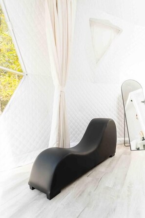 A modern room with a black lounge chair, a large mirror, and a view of trees through a window. - Private luxury dome with hot tub & fire pit. (Unionville)