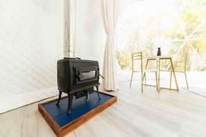 A wood stove in a room with a table and chairs, large windows, and a quilted wall.