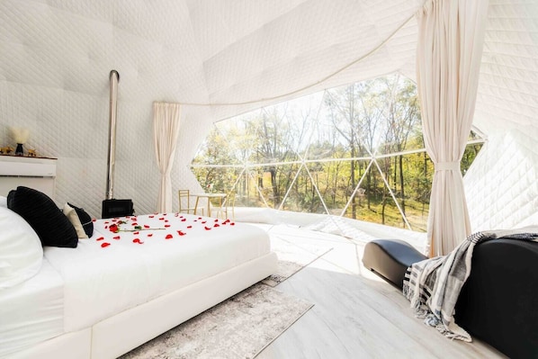Une chambre à coucher avec un lit, une table de chevet et une vue sur les arbres par une grande fenêtre.