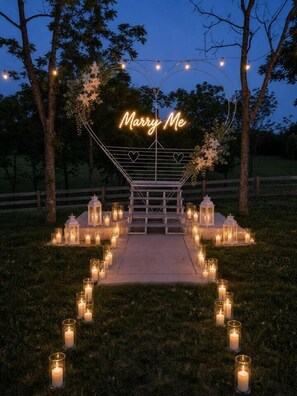 Une arche de mariage ornée d’un néon lumineux avec l’inscription « Veux-tu m’épouser ? », entourée de bougies et de lanternes.