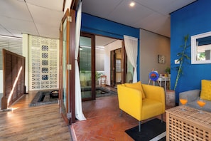 A modern living room with a yellow armchair, a glass door leading to a patio, and a blue accent wall. - Walk2Beach-FullKitchen-Fence-Garden-BBQ-Wifi-AC (Hua Hin)