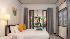 Una camera d'albergo con un letto, un comodino, una lampada, vista attraverso una porta in vetro e un quadro appeso al muro.