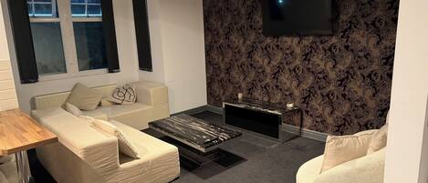A modern living room with a sofa, a coffee table, a TV mounted on the wall, and a window with curtains.