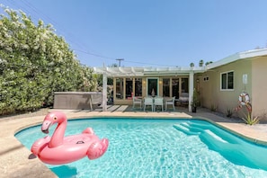 Ein Swimmingpool mit einem rosa Flamingo-Schwimmtier, eine überdachte Terrasse mit Stühlen und ein Gebäude mit Tür und Fenstern.