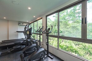 Un gimnasio con cintas de correr, bicicletas estáticas y una máquina de remo, con amplias ventanas que dan a zonas verdes.
