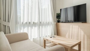 A modern living room with a sofa, a wooden coffee table, a flat-screen TV mounted on a wooden wall, and sheer curtains. - Beach 3 Mins Fantasea Resort Kamala C190 (Tambon Kamala)