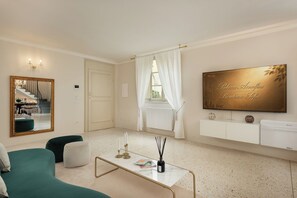 Ein Wohnzimmer mit einer Couch, einem Couchtisch, einem Spiegel, einem Fernseher und einem Fenster mit Vorhängen.