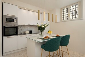 Eine moderne Küche mit weißen Schränken, einem eingebauten Backofen, einer Mikrowelle, einer Glasinsel und zwei grünen Stühlen.