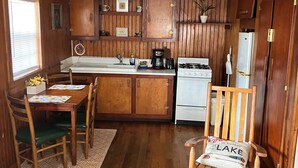 A kitchen with wooden cabinets, a sink, a stove, and a refrigerator. There is a dining table with chairs and a rug. - Cozy 1-bedroom cabin on Lake Hamilton in front of a private beach (Hot Springs)