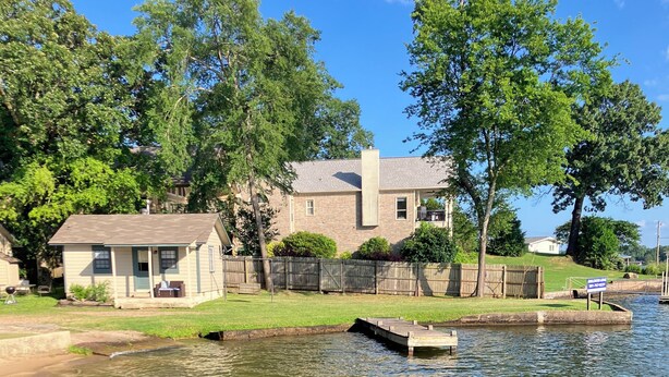A house with a dock extending into a calm body of water, surrounded by greenery and a clear sky. - Cozy 1-bedroom cabin on Lake Hamilton in front of a private beach (Hot Springs)