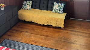 A room with a dark brown wooden wall, a black sofa with yellow and floral cushions, a ceiling fan, a window with curtains, and a wooden door. - Cozy 1-bedroom cabin on Lake Hamilton in front of a private beach (Hot Springs)