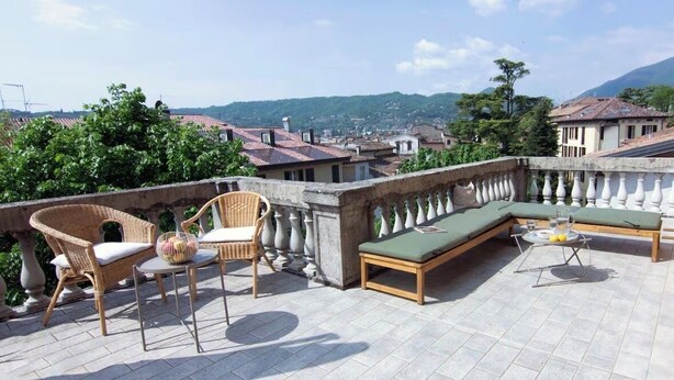 Eine Dachterrasse mit Korbstühlen, einer Couch und einem Tisch mit Glasplatte.