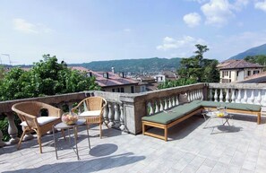 Terraço no telhado com cadeiras de vime, um sofá e uma mesa com tampo de vidro.