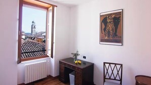 Ein Zimmer mit Fensterblick auf eine Stadtlandschaft, einem Heizkörper, einem Schreibtisch mit einer Vase und einem Poster an der Wand.