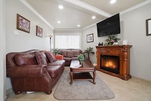 A living room with a brown leather sofa, a wooden coffee table, a fireplace, and a TV mounted on the wall. - Delightful Ocean Breeze 1-bedroom apartment in San Pedro (Los Angeles)