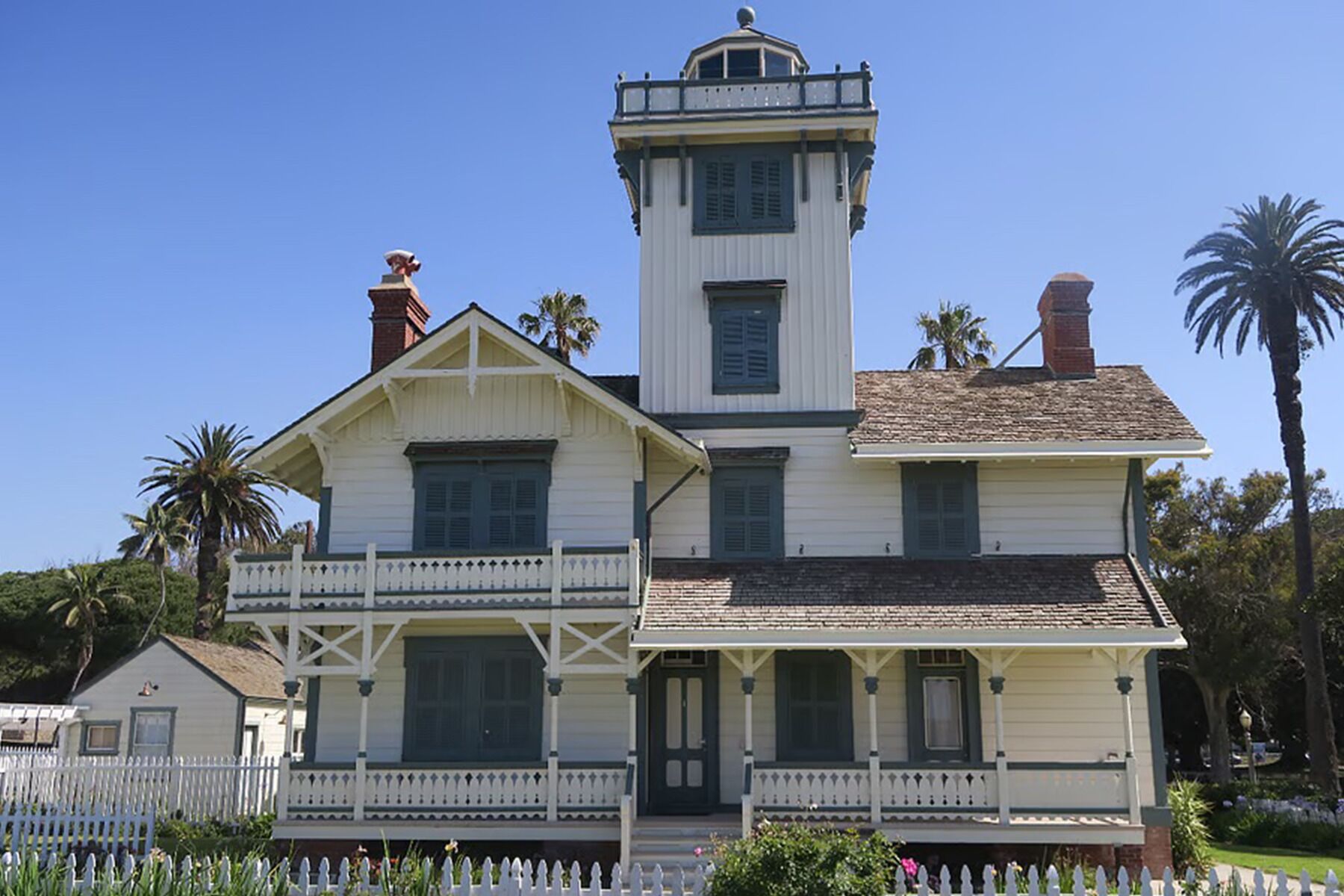 A two-story building with a prominent tower, a balcony, and a white picket fence.