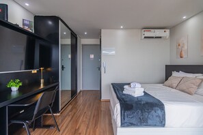A modern hotel room with a bed, bedside table, a desk with a chair, an air conditioning unit, and a small plant. - Excellent Studio in S o Paulo - Sp-a1107 (São Paulo)