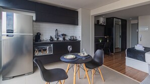 A modern kitchen with a built-in refrigerator, a dining area with two chairs and a small table, and a separate living area with a bed. - Excellent Studio in S o Paulo - Sp-a1107 (São Paulo)
