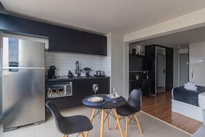 A modern kitchen with a built-in refrigerator, a dining area with two chairs and a small table, and a separate living area with a bed. - Excellent Studio in S o Paulo - Sp-a1107 (São Paulo)