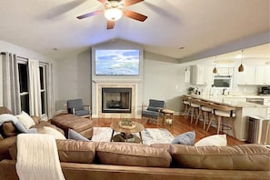 Ein Wohnzimmer mit Kamin, Fernseher, Deckenventilator und einer Küchenzeile mit Barhocker.