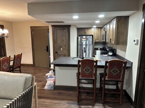 A modern kitchen with wooden cabinets, a stainless steel refrigerator, and a dining area with chairs and a table. - Great Smoky Mountains Resort  (Gatlinburg)
