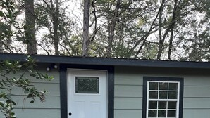 A small, single-story mobile home with a white front door, a small window, and a set of wooden steps leading up to the door.
