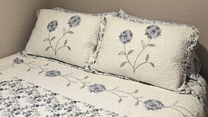 A bedroom with a bed, floral bedding, and a painting of sunflowers on the wall.