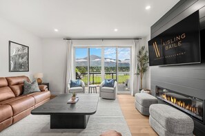 Un salon moderne avec un canapé en cuir, une table basse, une cheminée et une grande fenêtre donnant sur les montagnes.