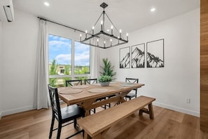 Un espace repas avec une table en bois, des bancs, un lustre et des œuvres d’art murales sur le thème de la montagne.