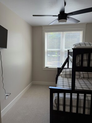 Ein Zimmer mit Etagenbett, Deckenventilator, Fenster mit Jalousien und einem an der Wand montierten Fernseher.