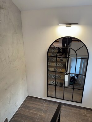 Ein Zimmer mit einem großen Bogen-Spiegel, einer Leuchte darüber und einer Wand mit Muster.
