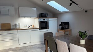 Een moderne keuken met witte kasten, een ingebouwde oven, een magnetron en een dakraam boven de eethoek.