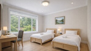 A hotel room with two beds, a desk, a chair, a window with a view of greenery, and a painting on the wall.