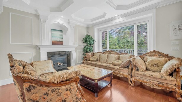 A spacious living room with a fireplace, ornate furniture, and a large window with blinds.
