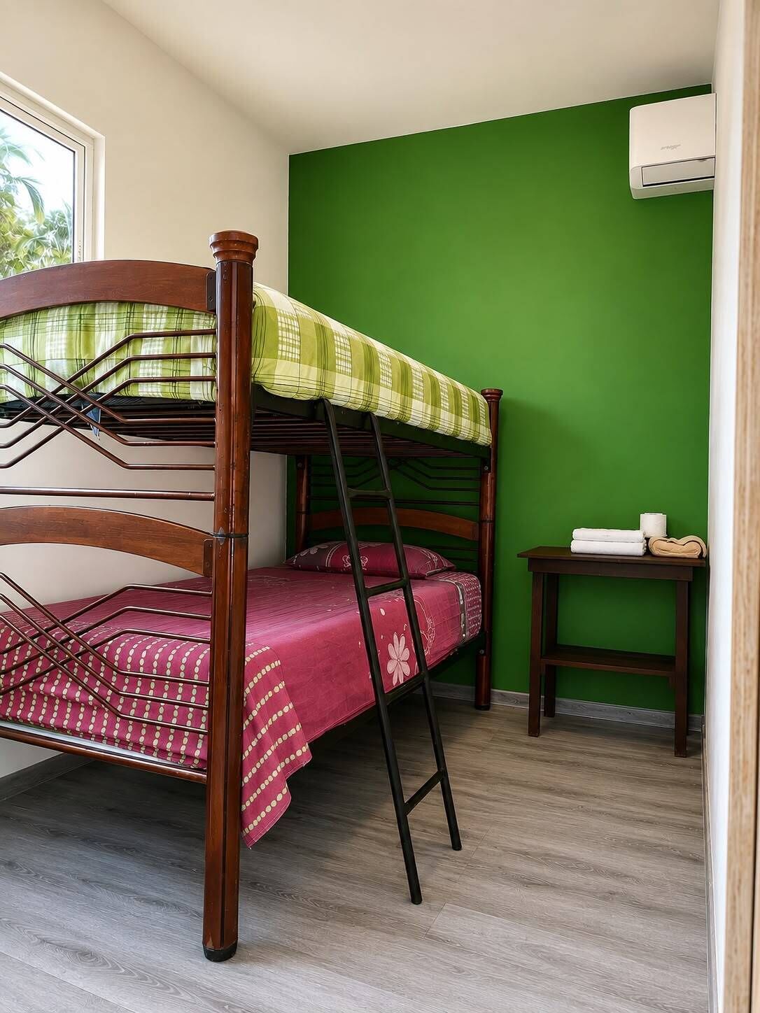 A bunk bed with a green wall and a small table beside it.