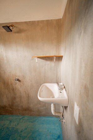 Un baño con un lavamanos blanco, una ducha y un estante de madera.