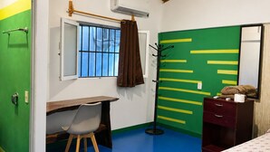 A room with a wooden ceiling, a desk with a chair, a bed, a dresser, and a window with a curtain.
