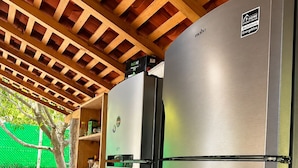 A stainless steel refrigerator with a digital display, a wooden ceiling, and a table with chairs.